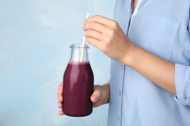 Photo of Woman with bottle of fresh acai drink and straw on light blue background, closeup