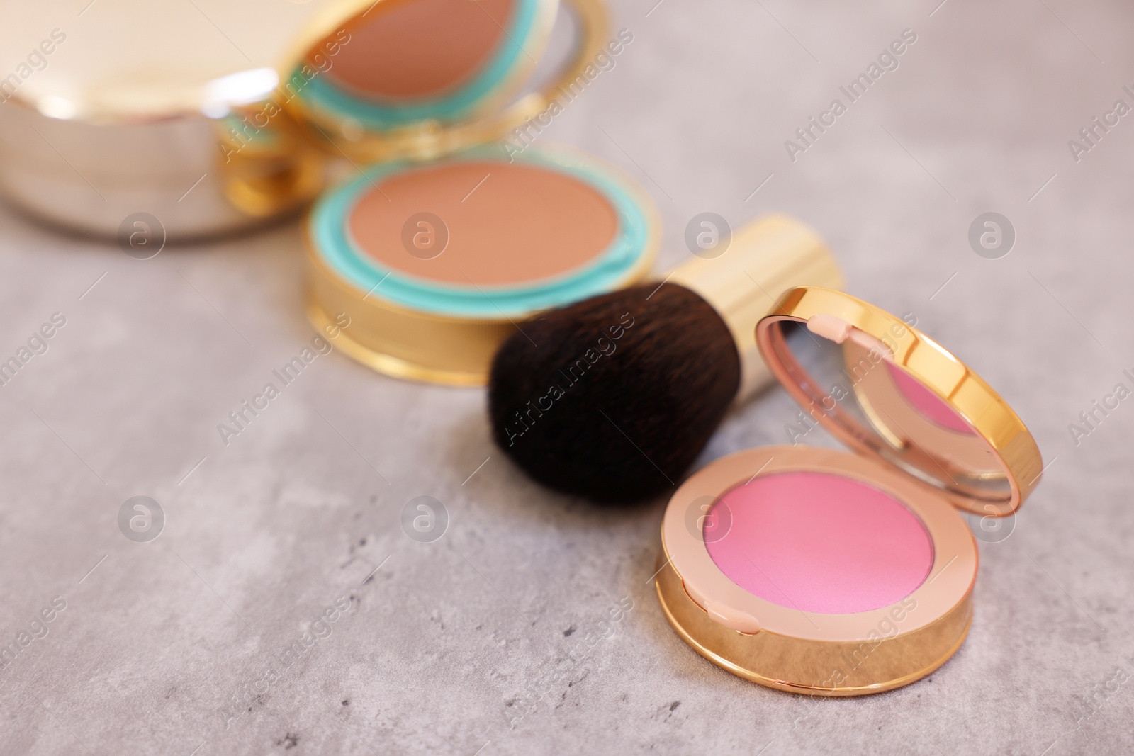 Photo of Face blusher and other cosmetic products on grey textured table, closeup