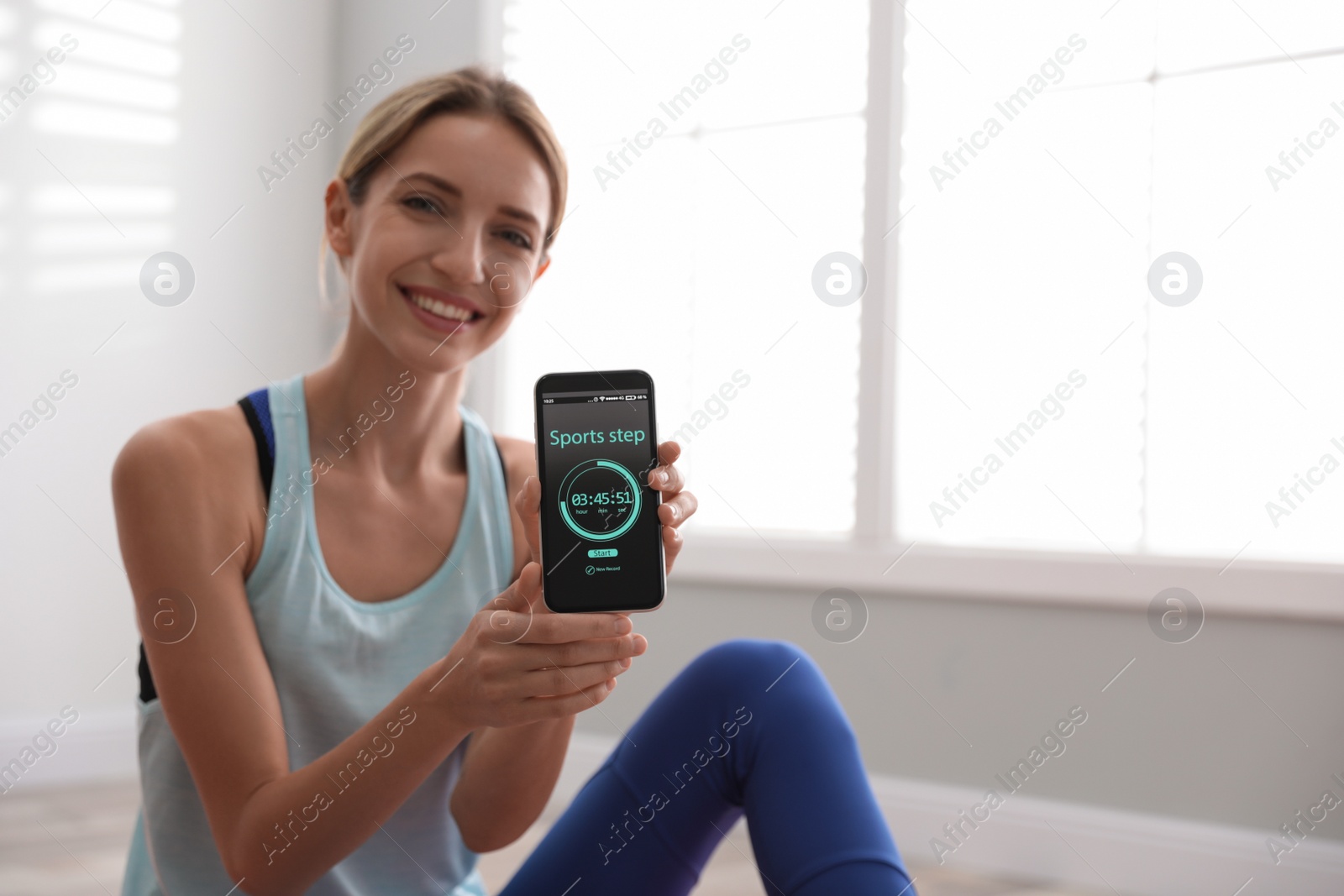 Photo of Young woman showing smartphone with fitness app indoors. Space for text