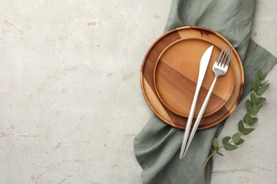 Photo of Stylish setting with cutlery, napkin, eucalyptus branch and plates on light table, top view. Space for text