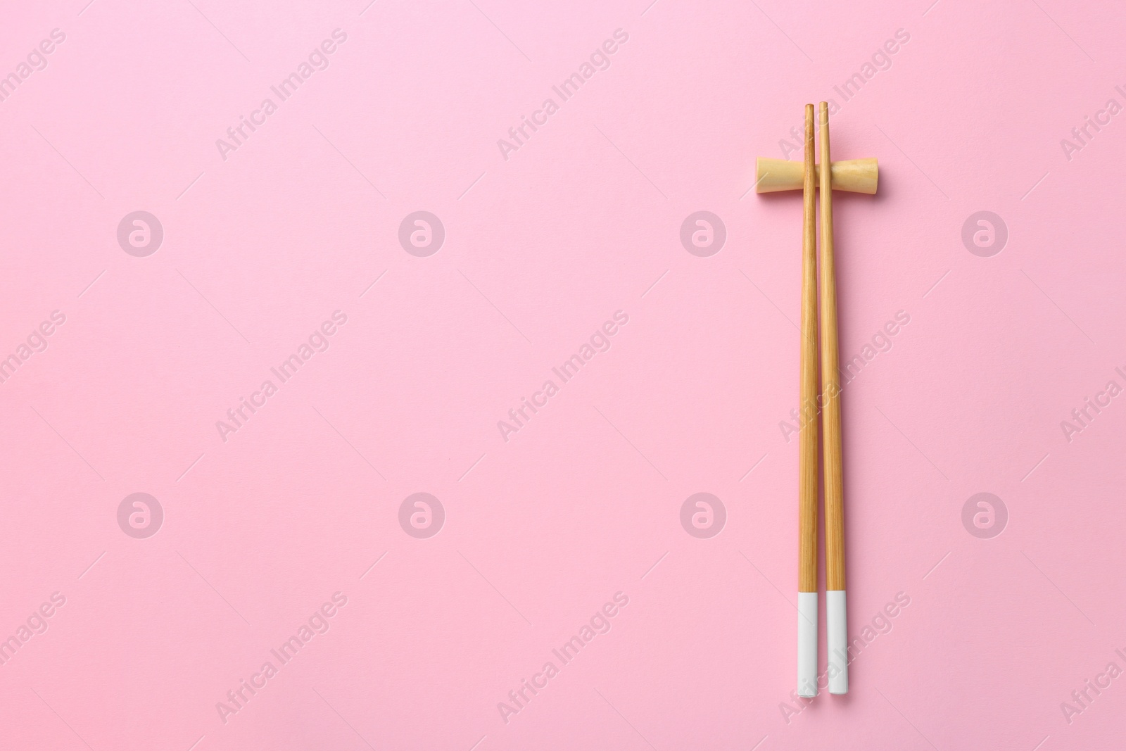 Photo of Pair of wooden chopsticks with rest on pink background, top view. Space for text