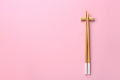 Photo of Pair of wooden chopsticks with rest on pink background, top view. Space for text