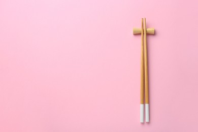 Pair of wooden chopsticks with rest on pink background, top view. Space for text