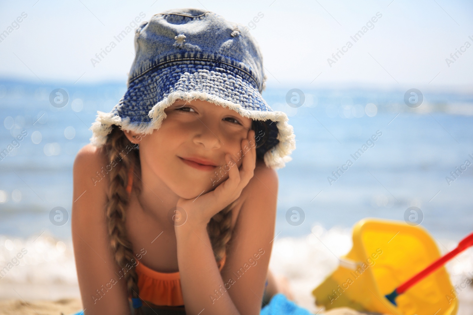 Photo of Little girl in stylish hat sunbathing on beach near sea