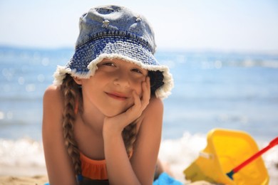 Photo of Little girl in stylish hat sunbathing on beach near sea