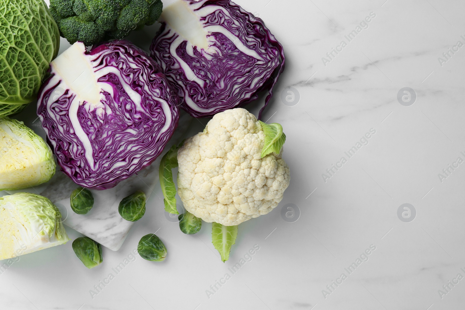 Photo of Many different types of cabbage on white marble table, flat lay. Space for text