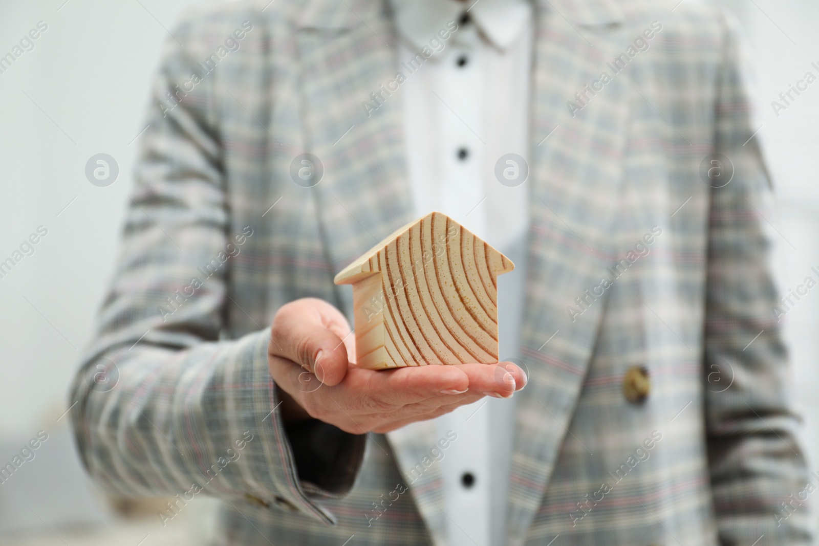 Photo of Real estate agent holding house figure indoors, closeup