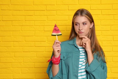 Photo of Beautiful girl with piece of watermelon near yellow brick wall. Space for text