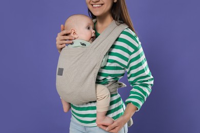 Photo of Mother holding her child in sling (baby carrier) on purple background, closeup