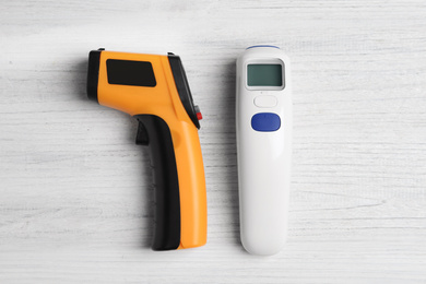 Modern non-contact infrared thermometers on white wooden background, flat lay