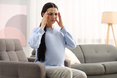 Photo of Pregnant woman suffering from headache on armchair at home