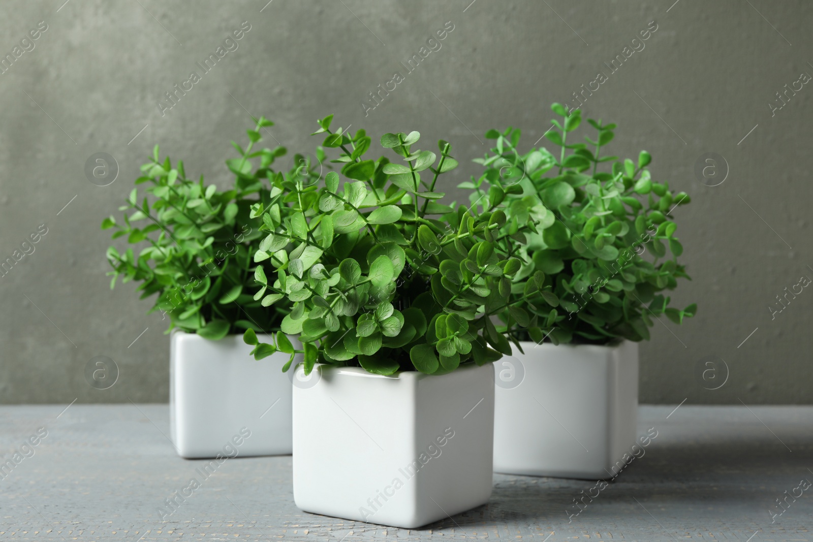 Photo of Artificial plants in white flower pots on grey wooden table