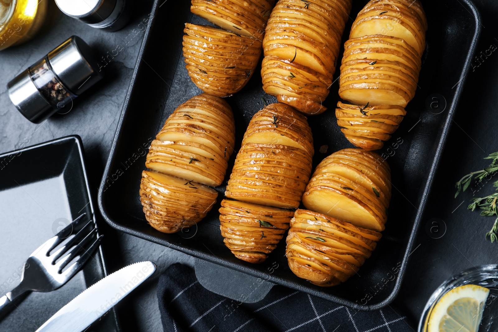 Photo of Delicious homemade Hasselback potatoes on black table, flat lay