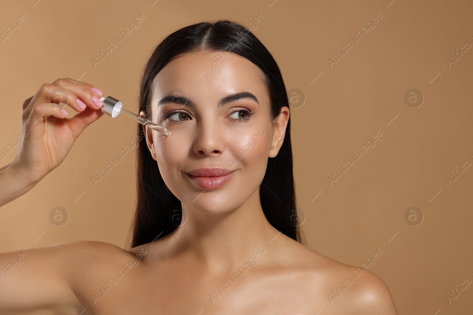 Photo of Beautiful young woman applying serum onto her face on beige background. Space for text