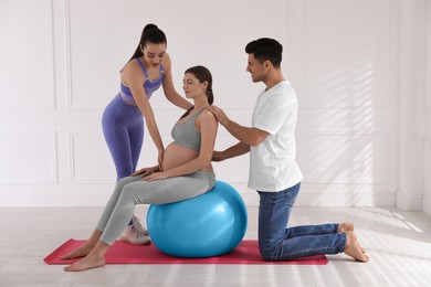 Pregnant woman and her husband working with trainer in gym. Preparation for child birth