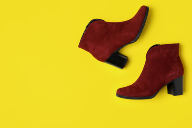 Stylish red female boots on yellow background, flat lay. Space for text