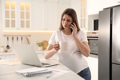 Pregnant woman working in kitchen at home. Maternity leave