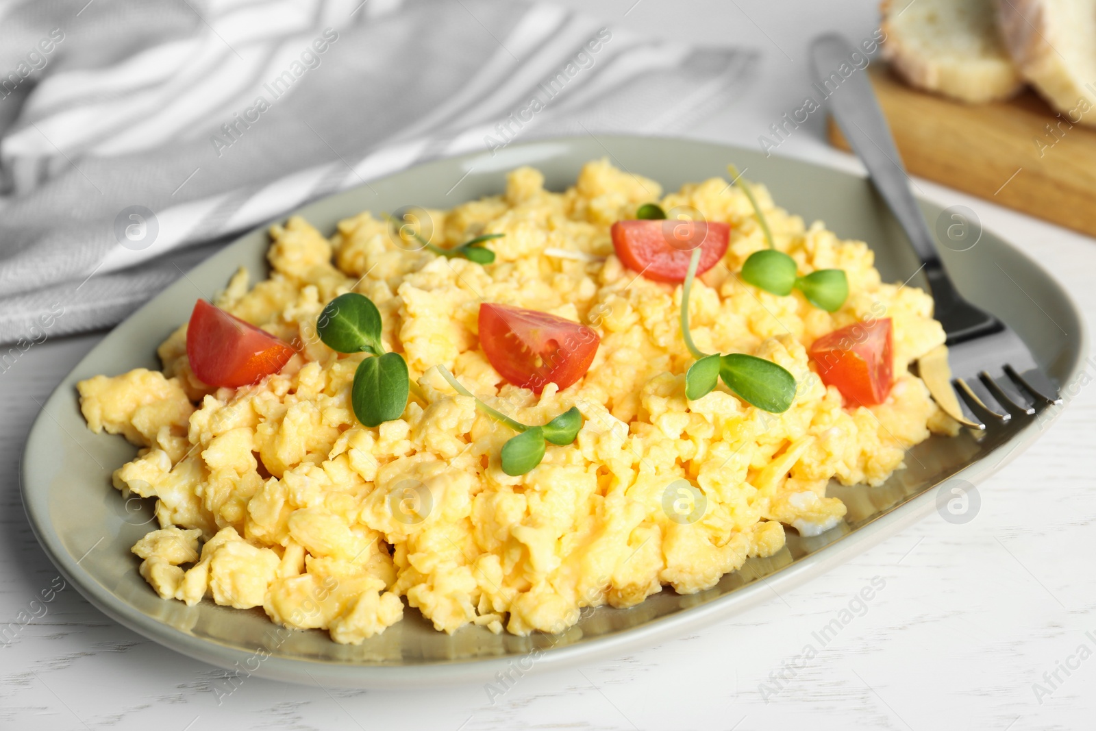 Photo of Tasty scrambled eggs with sprouts and cherry tomato served on white wooden table