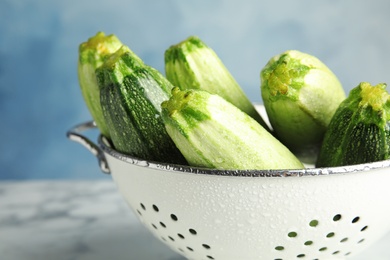 Colander with fresh ripe green zucchinis on marble table against blue background, closeup view