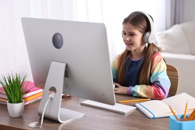 Photo of E-learning. Cute girl using computer and headphones during online lesson at table indoors