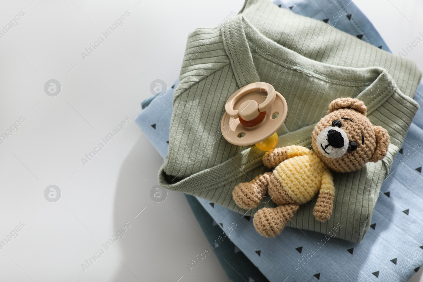 Photo of Baby clothes, pacifier and toy bear on light table, top view