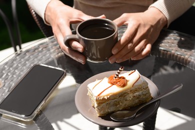 Photo of Woman with cup of coffee and tasty dessert at glass table outdoors, closeup