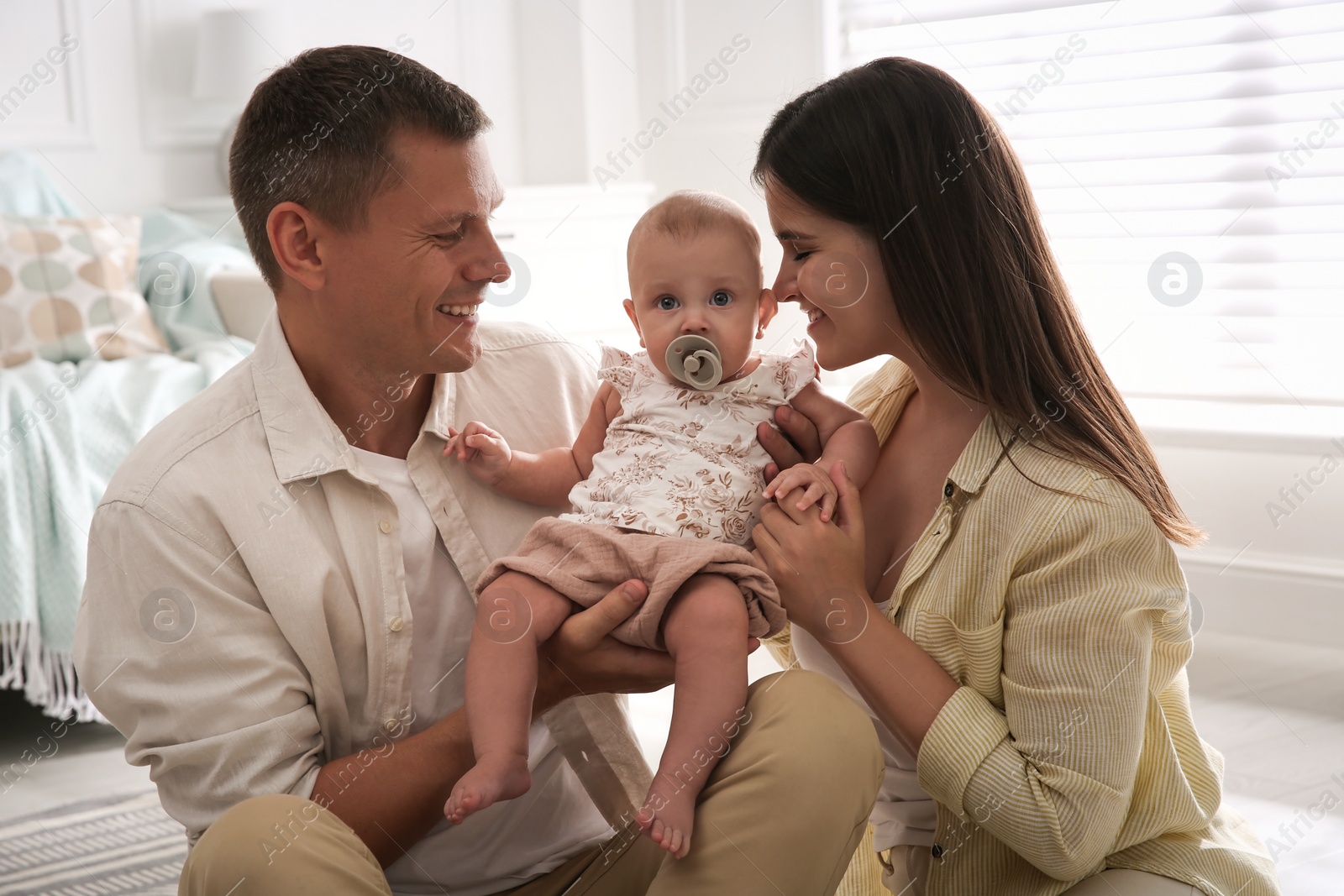 Photo of Happy couple holding their cute little baby with pacifier at home