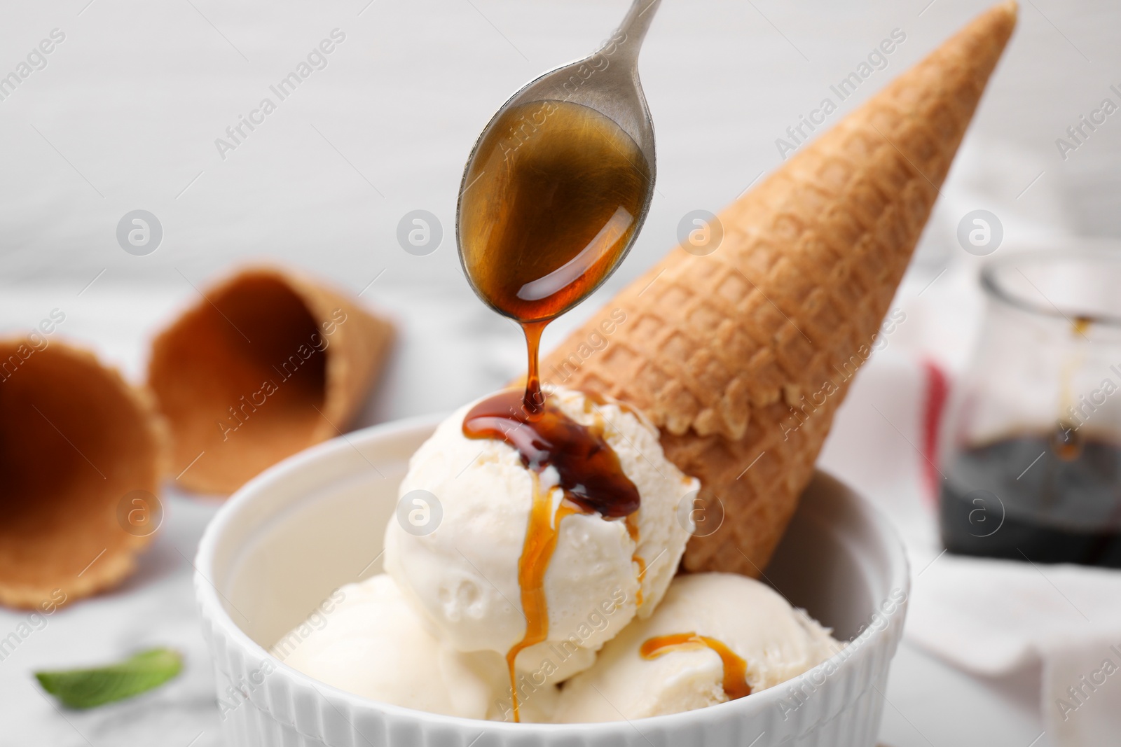 Photo of Pouring caramel sauce onto ice cream on table, closeup