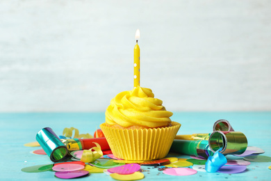 Delicious birthday cupcake with cream and burning candle on blue wooden background