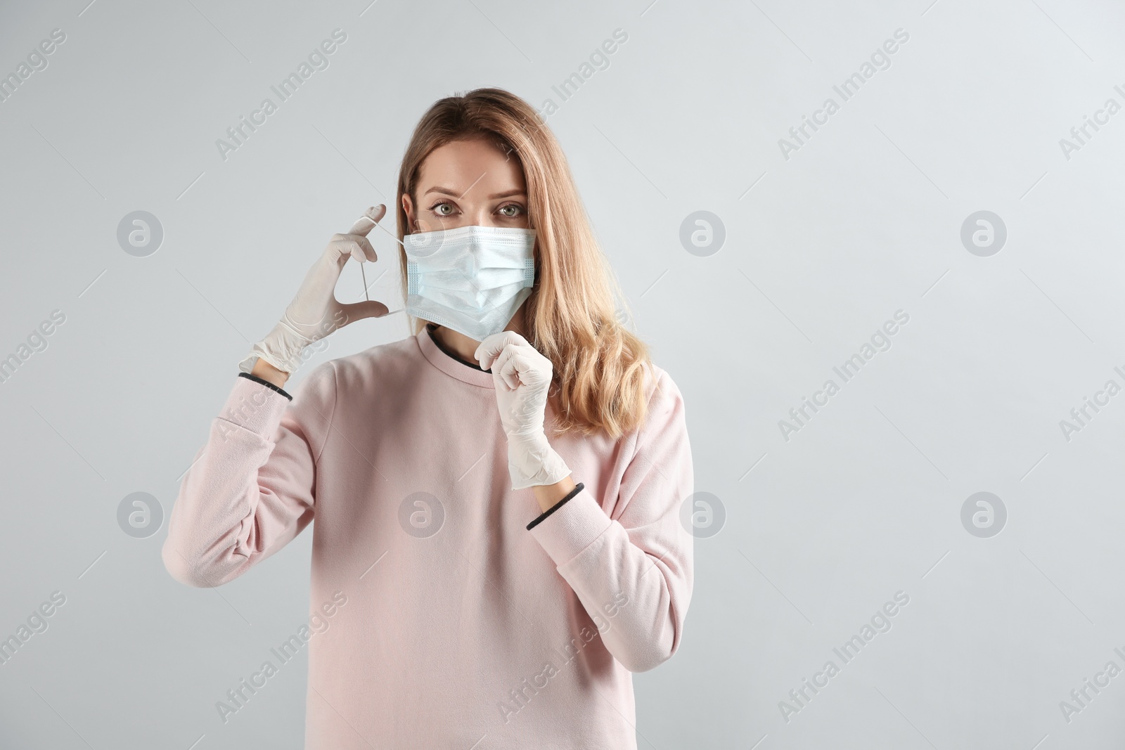 Photo of Young woman in medical gloves putting on protective mask against grey background. Space for text