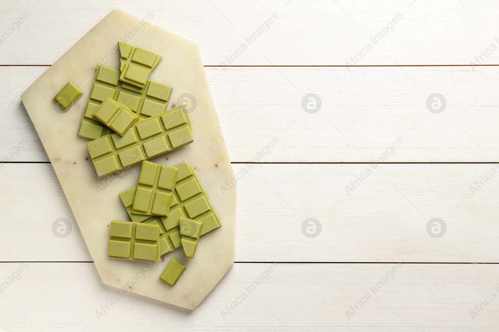 Photo of Pieces of tasty matcha chocolate bars on white wooden table, top view. Space for text