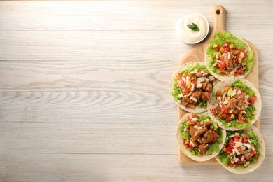 Delicious tacos with vegetables, meat and sauce on white wooden table, top view. Space for text