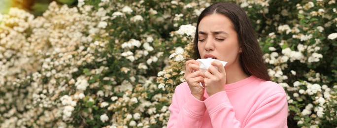 Image of Woman suffering from seasonal pollen allergy near blossoming tree on spring day. Banner design with space for text