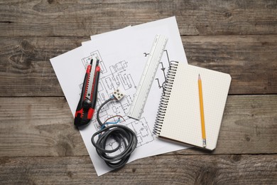 Photo of Wiring diagrams, wires, utility knife and office stationery on wooden table, flat lay