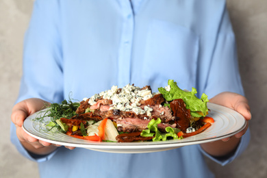 Photo of Woman holding plate with delicious salad on grey background, closeup