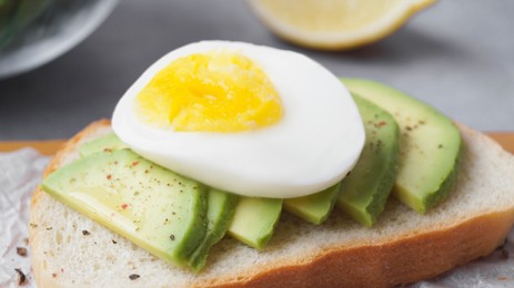 Photo of Delicious sandwich with boiled egg and pieces of avocado on table, closeup