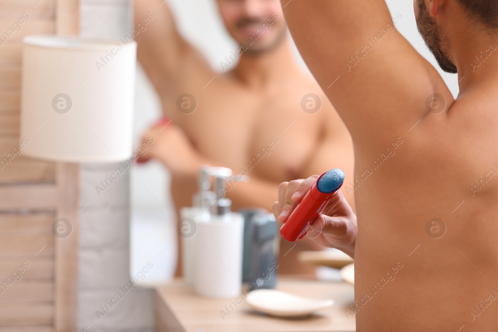 Photo of Handsome young man applying deodorant in bathroom. Space for text