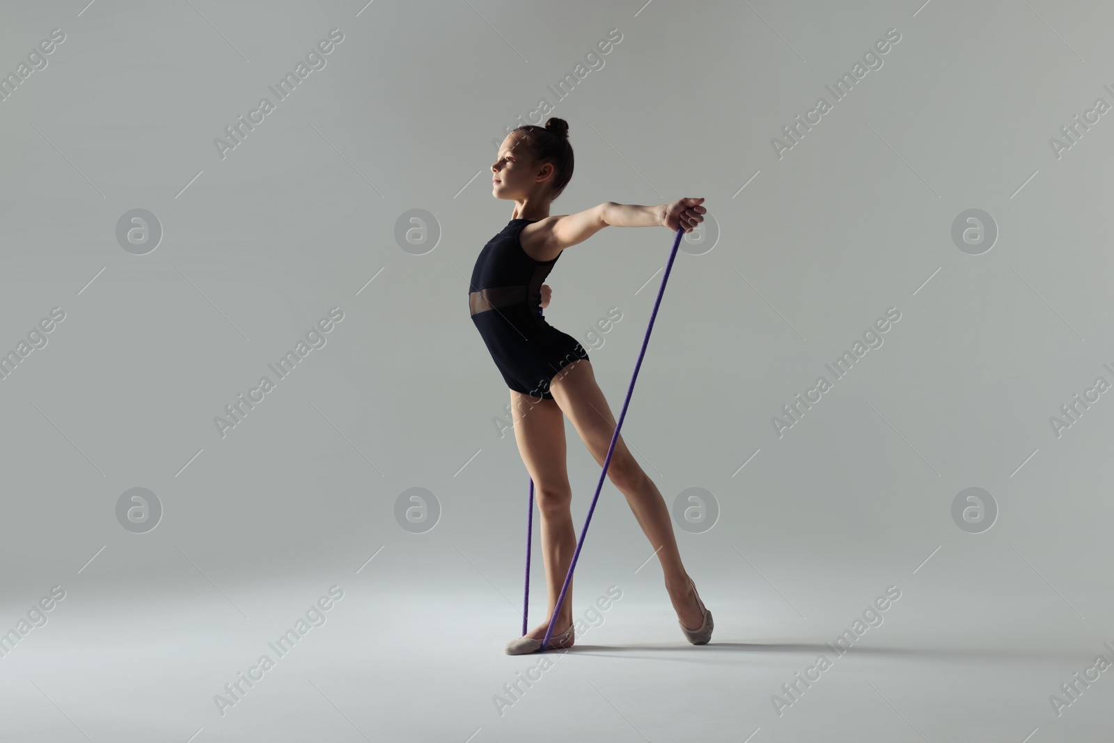 Photo of Cute little girl doing gymnastic exercise with rope on white background