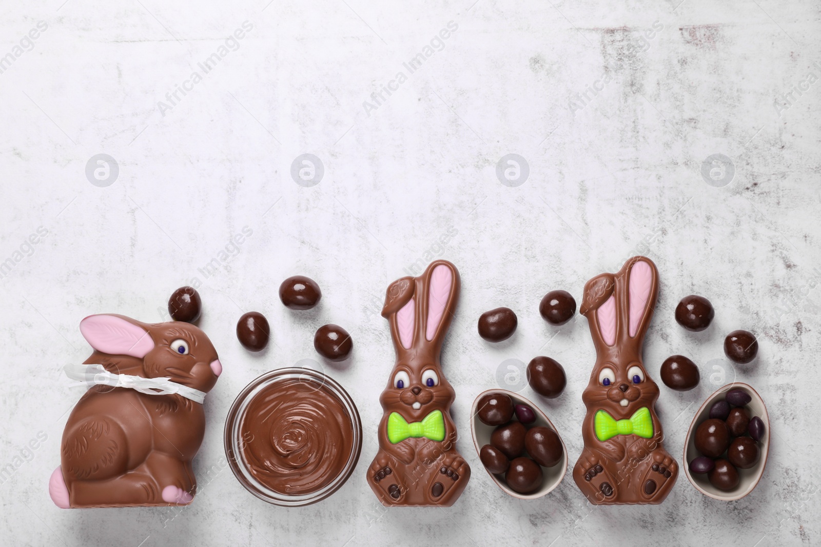 Photo of Flat lay composition with chocolate Easter bunnies, halved egg and candies on white textured table. Space for text