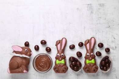 Flat lay composition with chocolate Easter bunnies, halved egg and candies on white textured table. Space for text