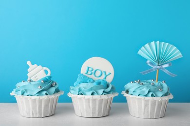 Photo of Baby shower cupcakes with toppers on white table against light blue background