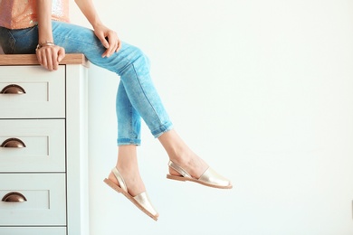 Photo of Young woman in elegant shoes sitting on chest of drawers, closeup