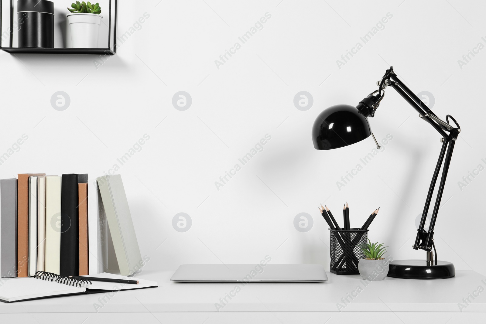 Photo of Cozy workspace with laptop, lamp and stationery on white desk at home