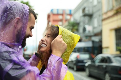 Photo of Young couple in raincoats enjoying time together on city street, space for text