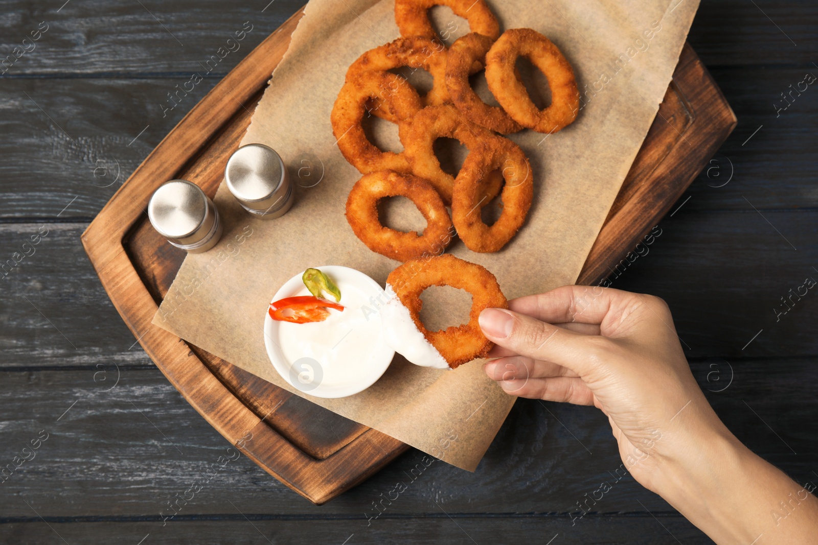 Photo of Woman dipping tasty onion ring into sauce at table