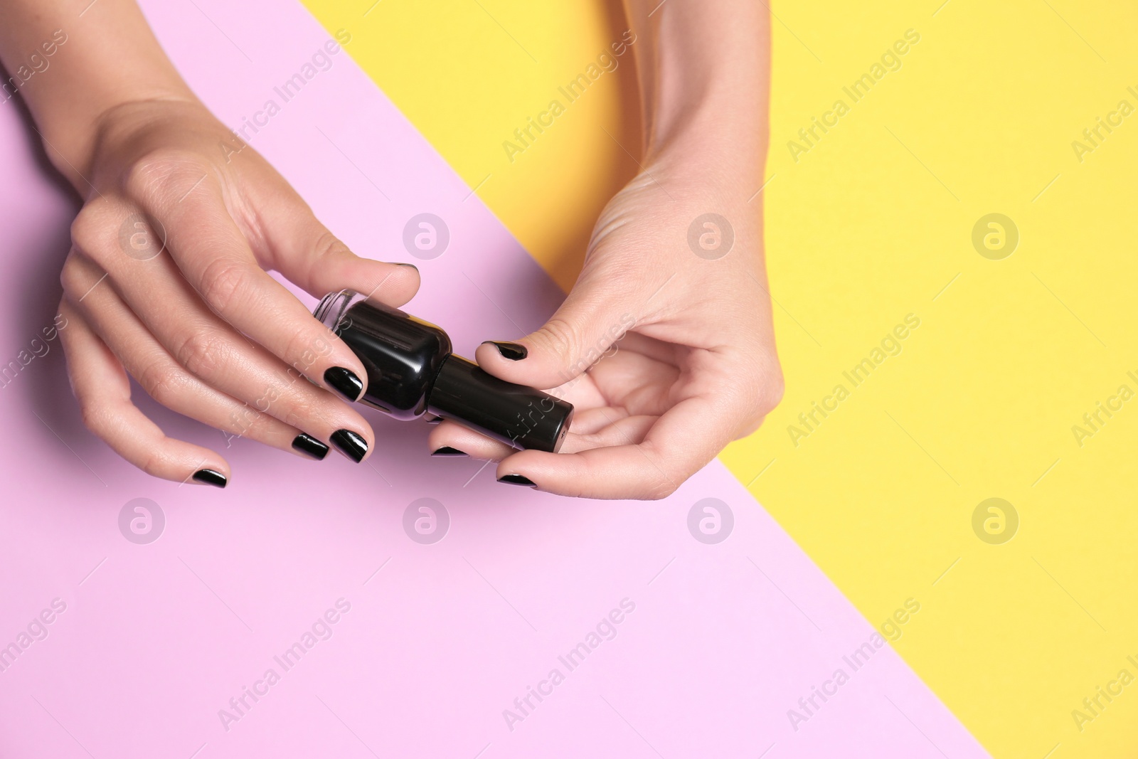 Photo of Woman holding bottle of black nail polish on color background, closeup. Space for text