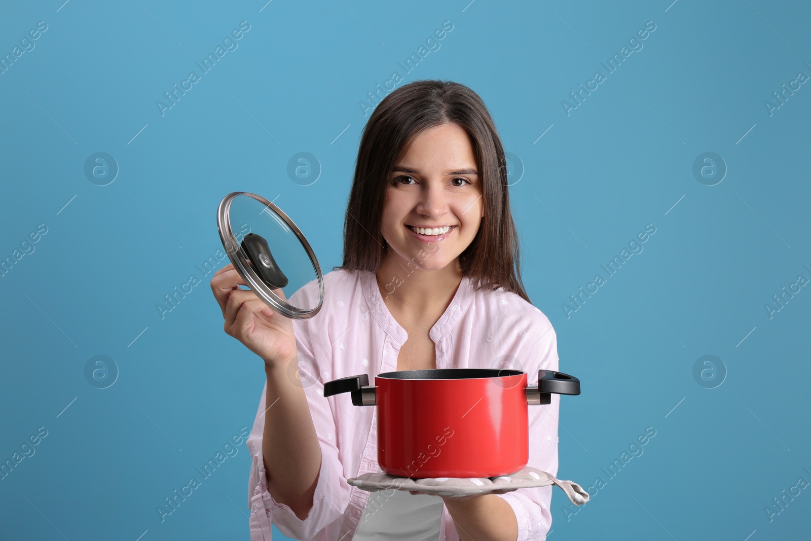 Photo of Happy young woman with cooking pot on light blue background