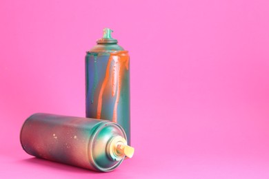 Photo of Two spray paint cans on pink background, space for text