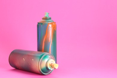 Two spray paint cans on pink background, space for text