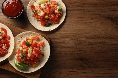 Photo of Delicious tacos with vegetables, lime and ketchup on wooden table, flat lay. Space for text